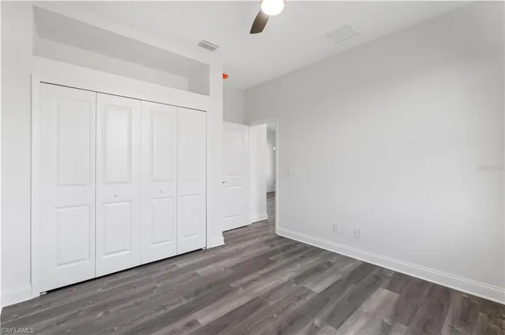 Unfurnished bedroom featuring wood finished floors, a closet, baseboards, and a ceiling fan