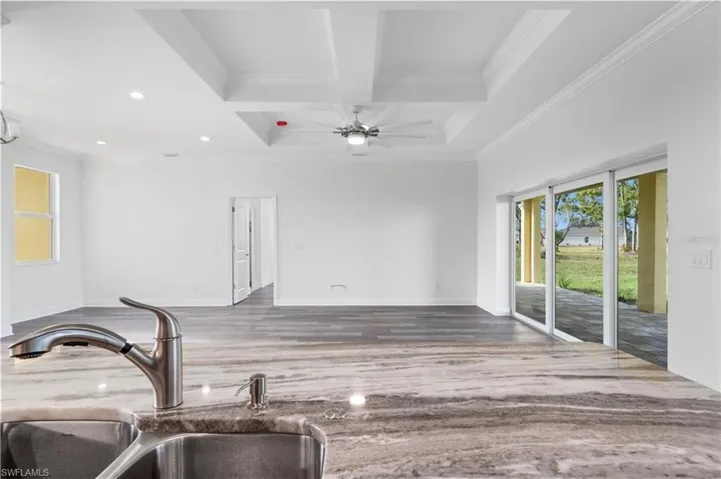Unfurnished living room with a sink, coffered ceiling, ornamental molding, beamed ceiling, and wood finished floors