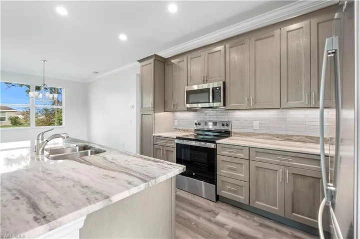Kitchen with appliances with stainless steel finishes, a sink, ornamental molding, light wood-style flooring, and tasteful backsplash