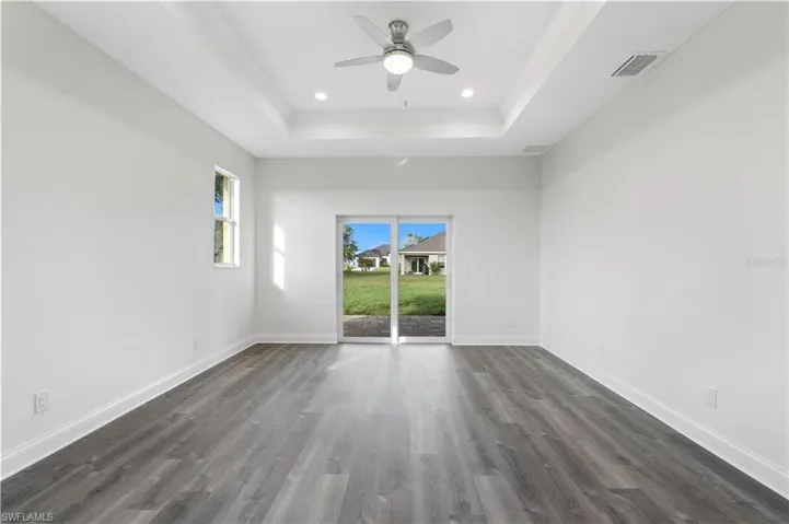 Unfurnished room with a tray ceiling, dark wood-type flooring, ceiling fan, ornamental molding, and baseboards