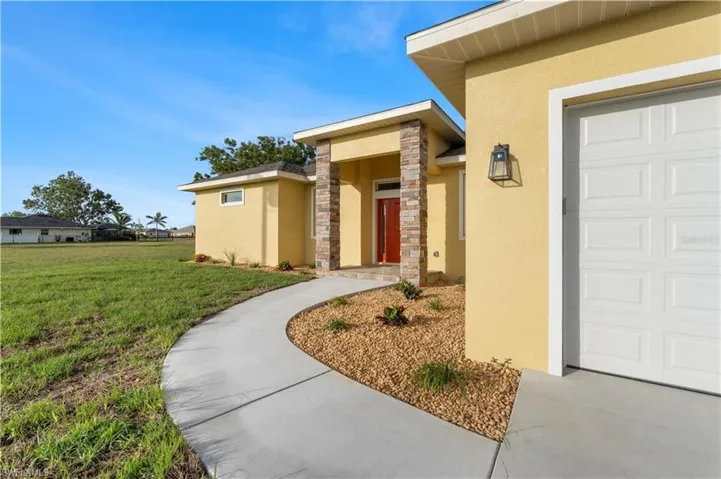 Entrance to property featuring stucco siding, a yard, stone siding, and a garage