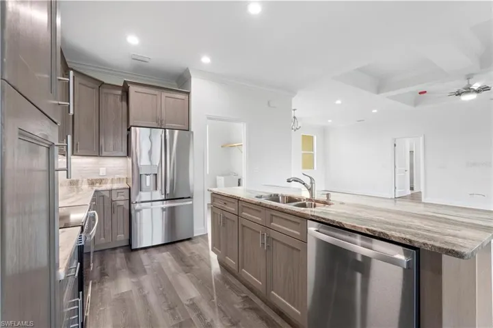 Kitchen with stainless steel appliances, a sink, ornamental molding, decorative backsplash, and light stone counters