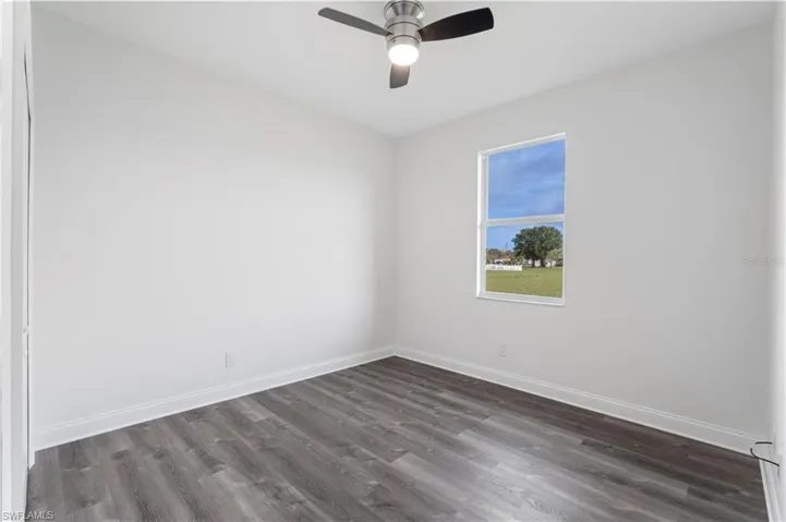 Unfurnished room featuring dark wood-type flooring, baseboards, and a ceiling fan
