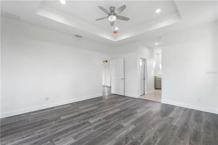 Unfurnished bedroom featuring a tray ceiling, recessed lighting, wood finished floors, baseboards, and crown molding