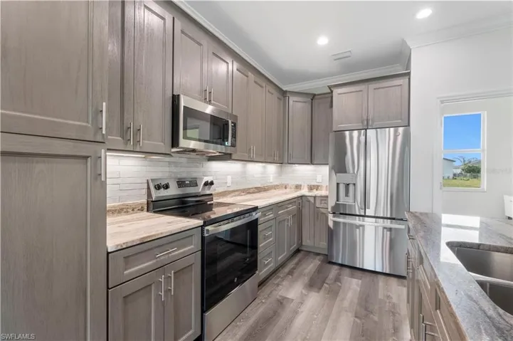 Kitchen featuring stainless steel appliances, gray cabinets, crown molding, light stone counters, and tasteful backsplash