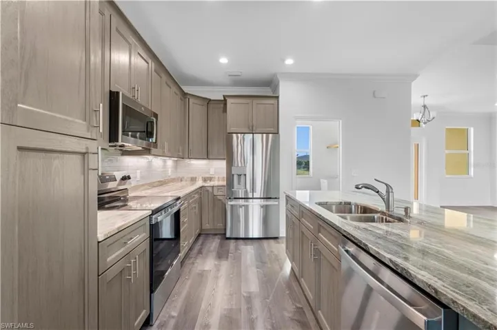 Kitchen featuring appliances with stainless steel finishes, a sink, ornamental molding, light stone counters, and tasteful backsplash