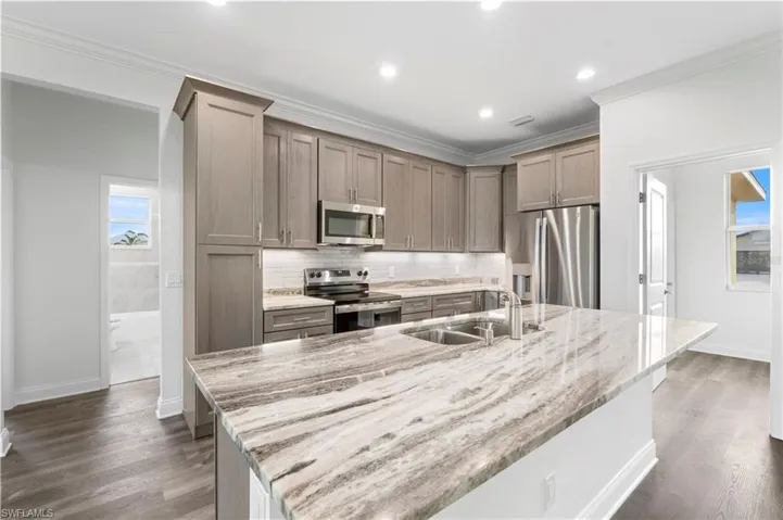 Kitchen featuring appliances with stainless steel finishes, a sink, backsplash, light stone counters, and dark wood-type flooring