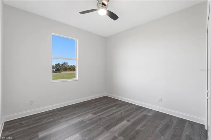 Spare room with dark wood-type flooring, baseboards, and ceiling fan