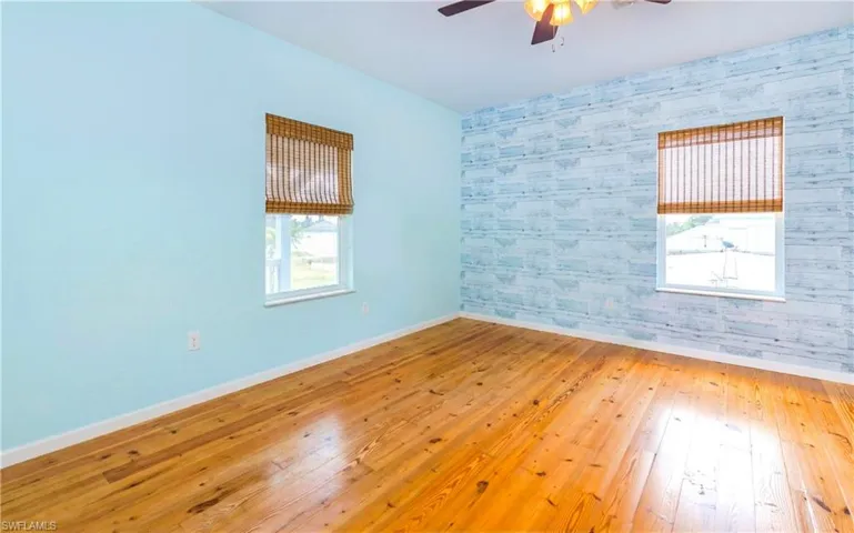 Unfurnished room with wallpapered walls, hardwood / wood-style floors, an accent wall, and a ceiling fan