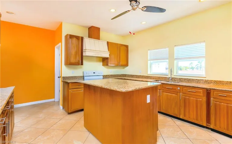 Kitchen with light tile patterned floors, brown cabinets, recessed lighting, white electric range, and custom range hood