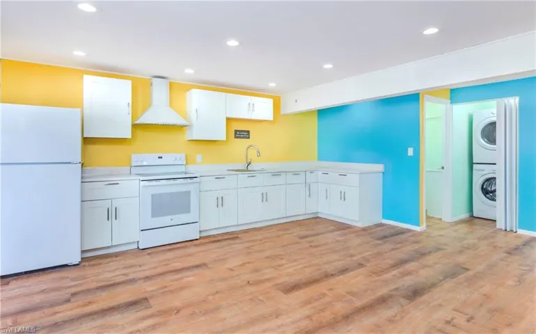 Kitchen featuring white appliances, white cabinetry, wall chimney exhaust hood, recessed lighting, and light countertops