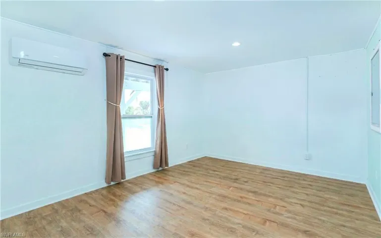Unfurnished room with wood finished floors, a wall mounted AC, and recessed lighting
