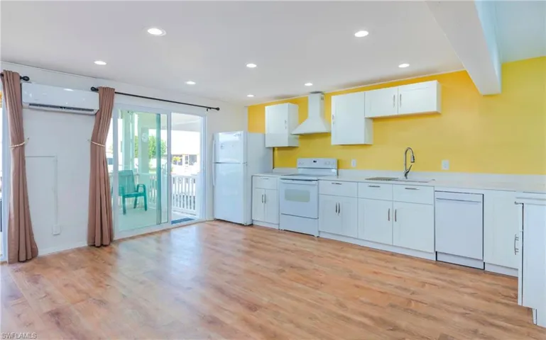 Kitchen featuring white cabinets, white appliances, wall chimney range hood, recessed lighting, and light wood-style flooring