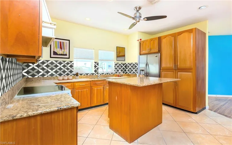 Kitchen with light stone countertops, brown cabinetry, stainless steel fridge, a kitchen island, and recessed lighting