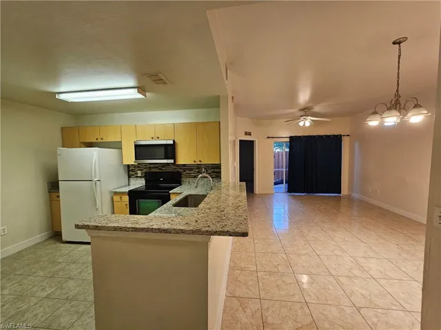 Kitchen featuring black range with electric cooktop, freestanding refrigerator, light stone counters, stainless steel microwave, and open floor plan
