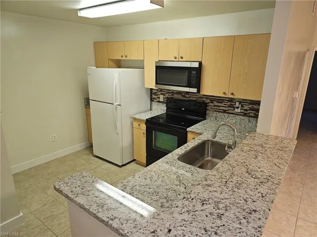 Kitchen featuring light stone countertops, electric range, stainless steel microwave, and decorative backsplash