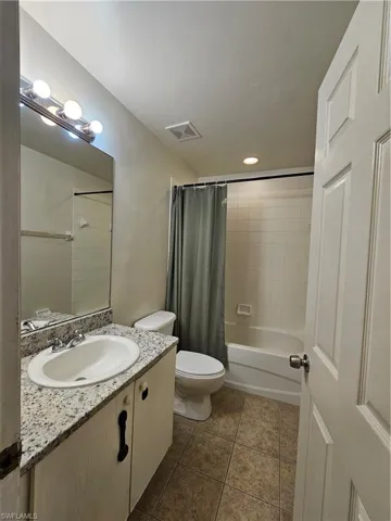 Full bathroom with vanity, shower / bath combination with curtain, and dark tile patterned floors