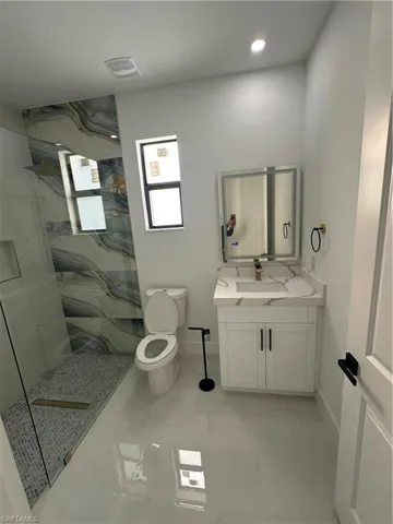 Bathroom with toilet, vanity, and tiled shower