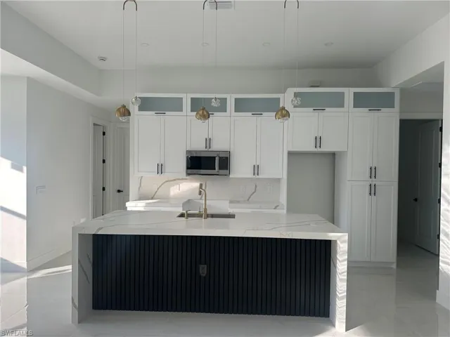 Kitchen with pendant lighting, light stone countertops, sink, and a kitchen island with sink