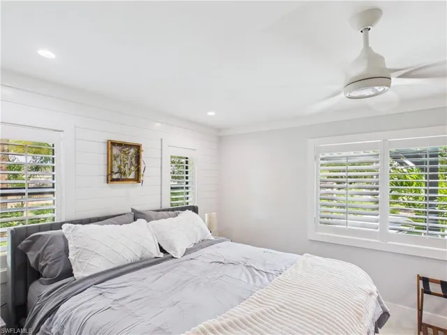 Bedroom featuring white plantation shutters, ceiling fan with integrated lighting, recessed lighting, and a shiplap accent wall