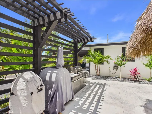 Expansive outdoor patio featuring a dark wood pergola, concrete flooring, and an outdoor kitchen area