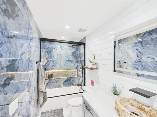 Bathroom with blue and white patterned wall tiling, a glass-enclosed shower with a recessed shelf, shiplap wall paneling, a vanity with a white countertop, and a natural wood vessel sink