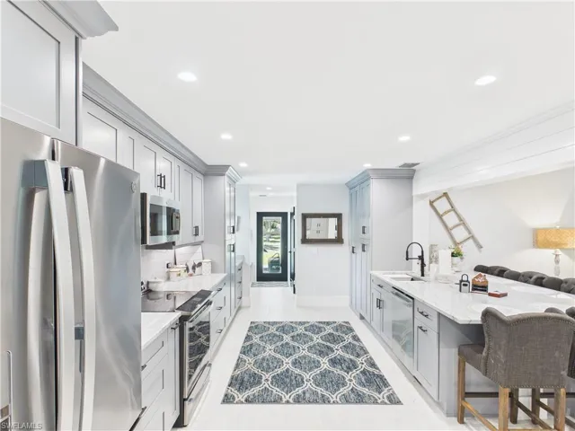 Bright kitchen featuring white flooring, gray cabinetry, stainless steel appliances, a center island with seating, and recessed lighting