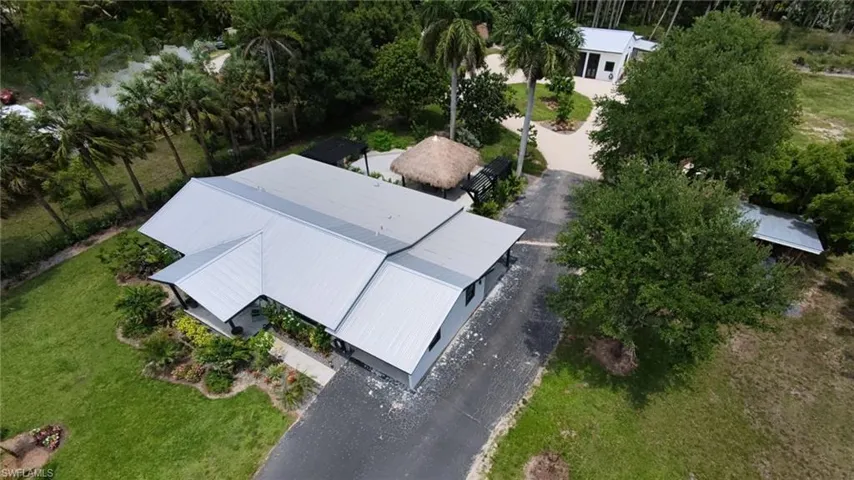 Expansive property featuring a contemporary residence with a metal roof, a separate detached structure, and a thatched-roof cabana