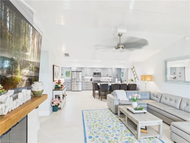 Open-concept living space featuring light-toned flooring, a wood-finish mantel, and a ceiling fan