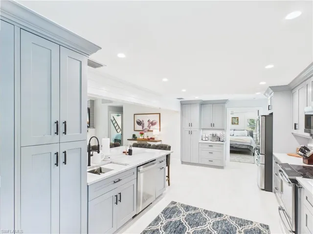 Modern kitchen featuring light gray shaker-style cabinetry, a central island with an integrated sink and dishwasher, sleek stainless steel appliances, and quartz countertops