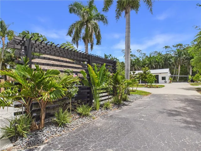 Paved driveway leading to a modern white structure featuring a dark facade and surrounding tropical landscaping