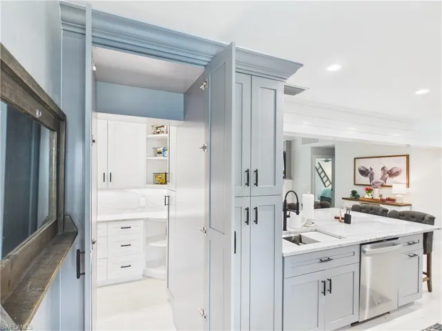 Gourmet kitchen featuring light gray cabinetry, built-in stainless steel appliances, a large center island with a sink and seating, and a walk-in pantry with white cabinetry and marble-patterned countertops