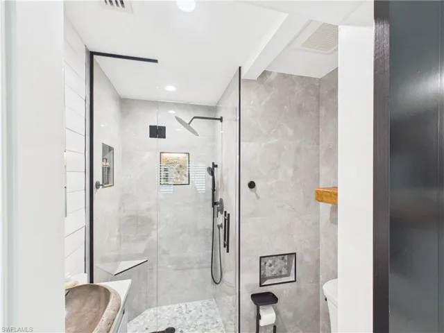 Bathroom featuring a glass-enclosed shower with matte black fixtures, full-height tile surround, and a built-in shower niche