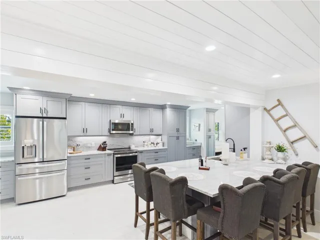 Gourmet kitchen featuring a large central island with seating, extensive gray cabinetry, stainless steel appliances, white countertops, and recessed lighting