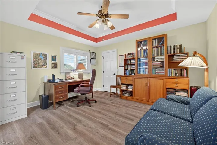 Office area with a raised ceiling, crown molding, ceiling fan, and light wood finished floors