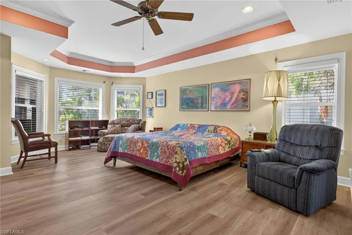 Bedroom featuring a raised ceiling, ornamental molding, light wood-type flooring, ceiling fan, and recessed lighting