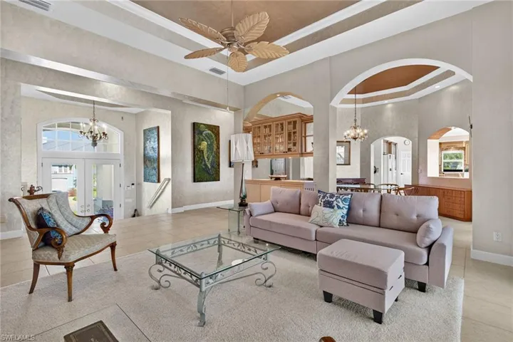 Living room with a raised ceiling, a chandelier, tile patterned floors, a high ceiling, and french doors