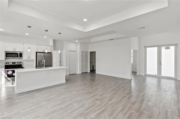 Kitchen with white cabinetry, a tray ceiling, pendant lighting, a center island with sink, and appliances with stainless steel finishes