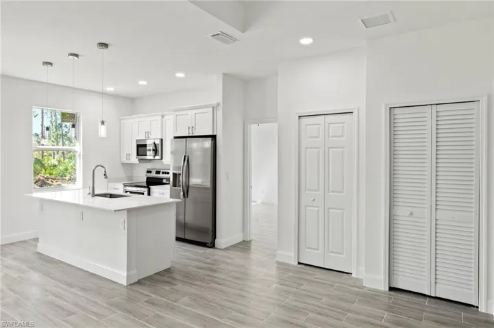 Kitchen with stainless steel appliances, pendant lighting, white cabinets, sink, and a center island with sink