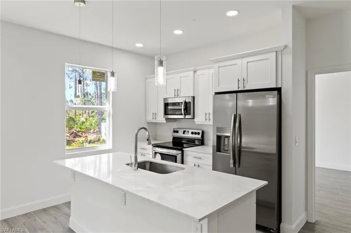 Kitchen with decorative light fixtures, sink, a center island with sink, appliances with stainless steel finishes, and light hardwood / wood-style flooring