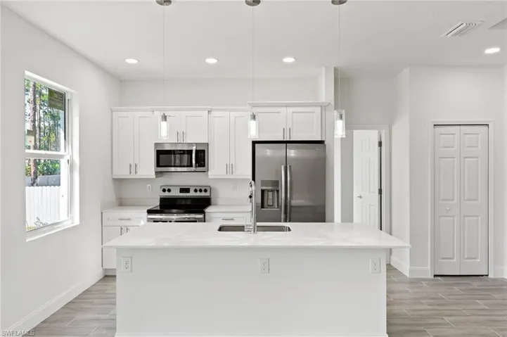 Kitchen with appliances with stainless steel finishes, white cabinets, sink, pendant lighting, and an island with sink