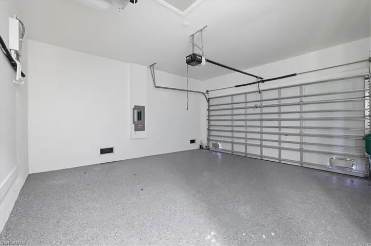 Spacious garage featuring a durable epoxy-coated floor, automatic garage door opener, and a wall-mounted electrical panel