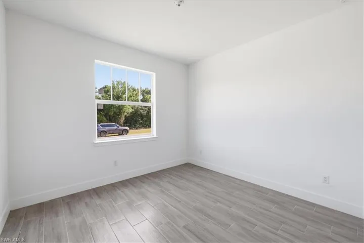 Bright interior space featuring a window with white trim, wood-look plank flooring, and a neutral white color palette