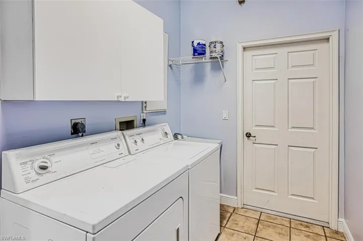 Laundry area with light tile patterned floors, cabinets, and washing machine and dryer