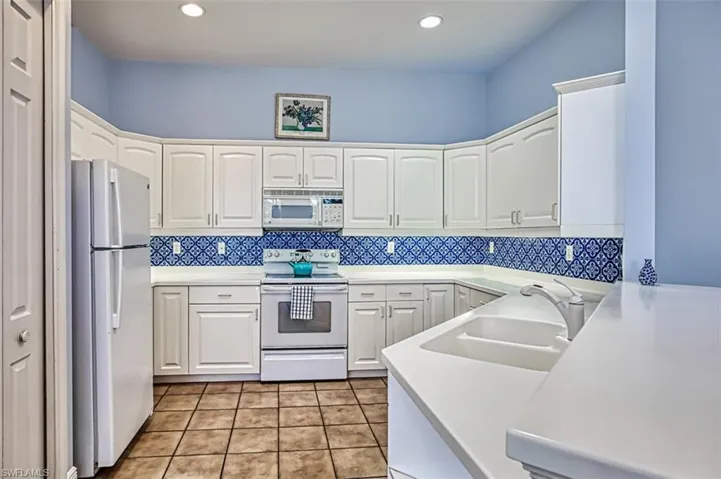 Kitchen with white cabinets, light tile patterned floors, white appliances, sink, and tasteful backsplash