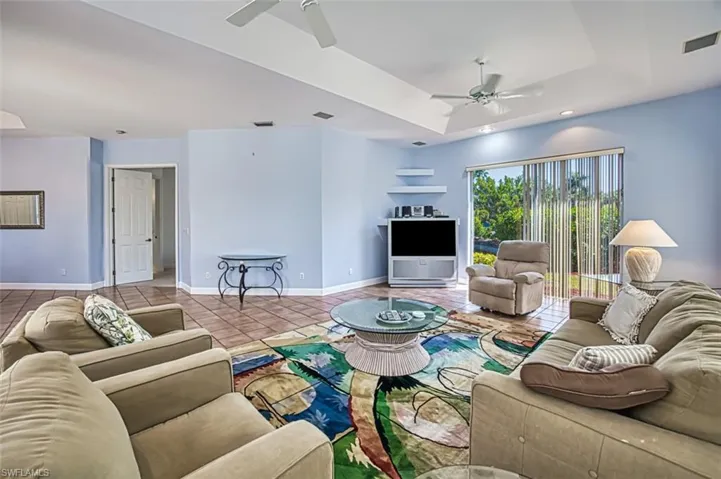 Living room with a tray ceiling, ceiling fan, and light tile patterned flooring