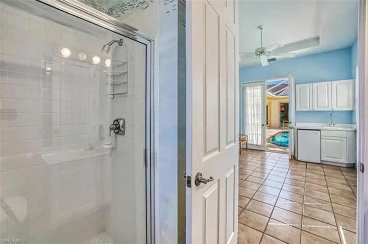 Bathroom featuring tile patterned flooring, ceiling fan, a shower with door, and vanity