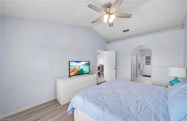 Bedroom featuring light wood-style floors, vaulted ceiling, a ceiling fan, multiple windows, and arched walkways
