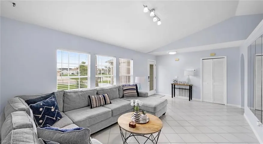 Living area with vaulted ceiling, light tile patterned floors, and rail lighting