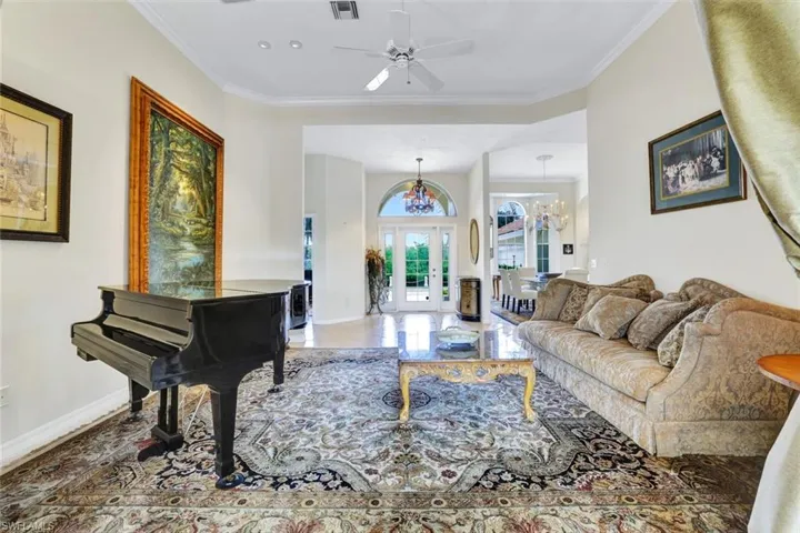 Living room view towards front entry featuring tile patterned floors, crown molding, and a notable chandelier.